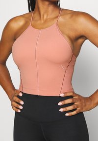 Růžový bezešvý crop top na halter s tenkými ramínky, přiléhavý design a kontrastní švy. V kombinaci s černými legínami s vysokým pasem.