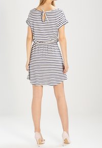 Robe rayée en blanc et marine avec une coupe décontractée, des manches courtes et un détail noué en découpe au dos ; taille élastique avec une ceinture.
