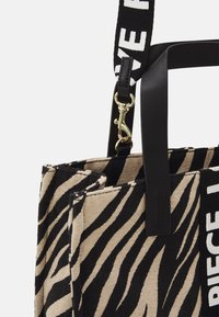 Sac fourre-tout en tissu à motif zèbre avec des accents en cuir noir et une bandoulière de marque. Il présente un fermoir doré et un design structuré.