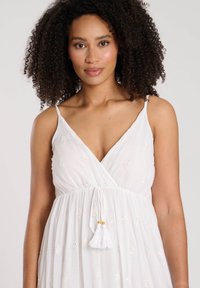 Witte maxi-jurk met een v-hals en verstelbare spaghettibandjes. Bevat geborduurde diamanten patronen en een taille met trekkoord en franjes.