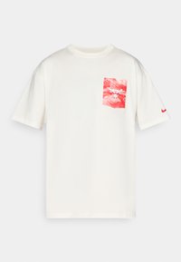 Cremefarvet bomulds t-shirt med en rød og hvid grafisk lomme med et tyr-logo og en lille rød Nike swoosh på venstre ærme.