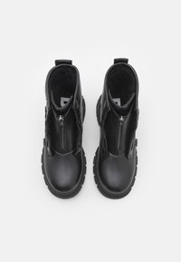 Crne gležnjače od kože, s dvostrukim patentnim zatvaranjem, debelim gumastim potplatom i glatkom teksturom. Namijenjene za kombiniranu upotrebu.