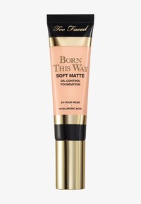Fond de teint Soft Matte Born This Way de Too Faced dans un flacon transparent, couleur pêche, avec des accents dorés et noirs, équipé d'un distributeur à pompe.