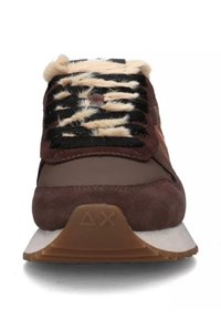 Zapatilla deportiva de ante marrón con una suela blanca gruesa, que presenta cordones en negro y crema, y acentos de textura suave alrededor del tobillo.