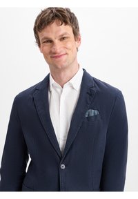 Navyblazer aus strukturiertem Stoff mit einem einzelnen Knopf, Reverskragen und einem Einstecktuch mit Streifen. Darunter ein weißes Hemd.