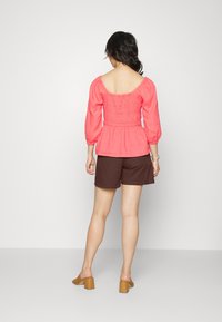 Korálově růžový peplum top s elastickým smockováním, dlouhými puff rukávy, spárovaný s hnědými šortkami a béžovými muly na blokovém podpatku.
