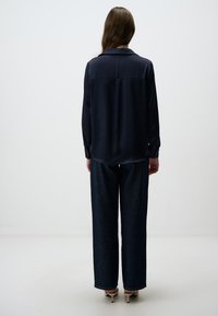 Navy zijden blouse met een rugplooitje, lange mouwen en geknoopte manchetten, gecombineerd met brede donkere spijkerbroek en puntige hakken.