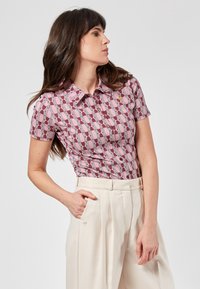 Camicia a maniche corte con un motivo geometrico rosa e accenti bianchi; dotata di colletto e bottoni, realizzata in tessuto morbido.