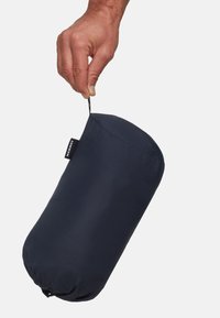 Una mano che tiene un sacchetto Mammut nero per il trasporto tramite il suo anello di apertura su uno sfondo bianco.