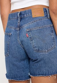Gros plan d'une personne portant un short en jean bleu Levi's avec des bords effilochés et un top court blanc.