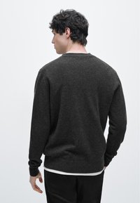 Tmavě šedý pletený svetr s dlouhými rukávy, kulatým výstřihem a žebrovanými manžetami. Jednoduchá, texturovaná látka s neformálním střihem.