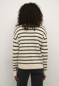Maglione crema con righe orizzontali nere, texture morbida, maniche lunghe e vestibilità rilassata, abbinato a jeans scuri. Design semplice e classico.