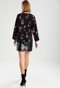 Chemise noire avec imprimé floral en rose et blanc, associée à une mini-jupe noire brillante. Manches longues, coupe décontractée, texture lisse.