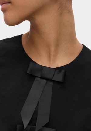 Zwarte top met een ronde halslijn en een opvallende zwart satijnen strikdetail aan de voorkant, gemaakt van een gladde, matte stof.