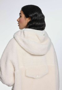 Kremowy, oversize hoodie wykonany z miękkiego, teksturowanego polaru, z dużym kapturem, prążkowanymi mankietami i zapinaną na guziki tylną kieszenią.