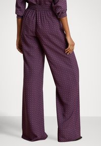 Vide bukser i lilla stoff med et geometrisk mønster i rosa og hvitt. Elastisk midjebånd for komfort. Jevn tekstur.