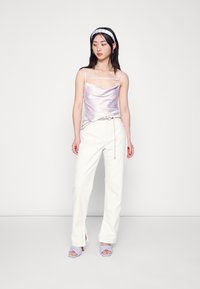 Camisola de cetim lilás com alças finas, combinada com calças largas brancas com detalhes em corrente e sandálias de tiras lilás claro.