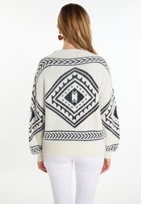 Maglione lavorato a maglia color crema con motivi geometrici neri, maniche oversize e vestibilità rilassata. Tessuto morbido con polsini e orlo a coste.