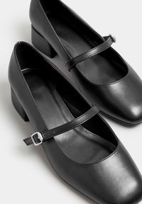 Svarta läder Mary Jane-skor har en rund tå, ett rem med silverdetalj och en låg blockklack. Slät yta genom hela skon.