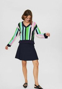 Pulover iz pletenine z večbarvnimi navpičnimi črtami v zeleni, roza in modri barvi, z V-izrezom in dolgimi rokavi, v kombinaciji s temno krilom.