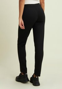 Pantaloni sportivi neri con una texture liscia, taglio aderente e vita elastica, abbinati a scarpe sportive nere.