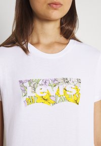 White cotton t-shirt featuring a colorful floral graphic with yellow and purple flowers, and the "Levi's" logo in bold white letters.