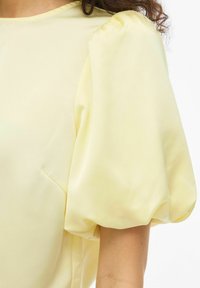 Blouse jaune à manches ballon, confectionnée en tissu lisse. Les manches sont volumineuses et le modèle présente un col rond classique.