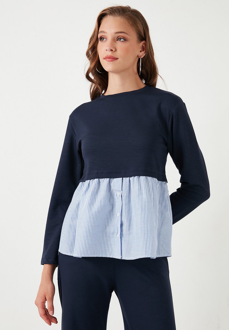 Maglietta a maniche lunghe blu navy con scollo rotondo; presenta un pannello di tessuto a righe blu e bianche in vita, evidenziato da bottoni.