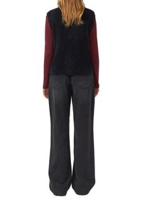 Schwarze Strickweste mit strukturiertem Finish, über einem burgunderfarbenen Langarmoberteil getragen, kombiniert mit weit geschnittenen schwarzen Jeans.