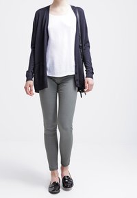 Mörkblå cardigan, vit topp och grå slim-fit byxor. Svarta loafers har en glänsande finish. Cardiganen har en avslappnad passform och öppen front.