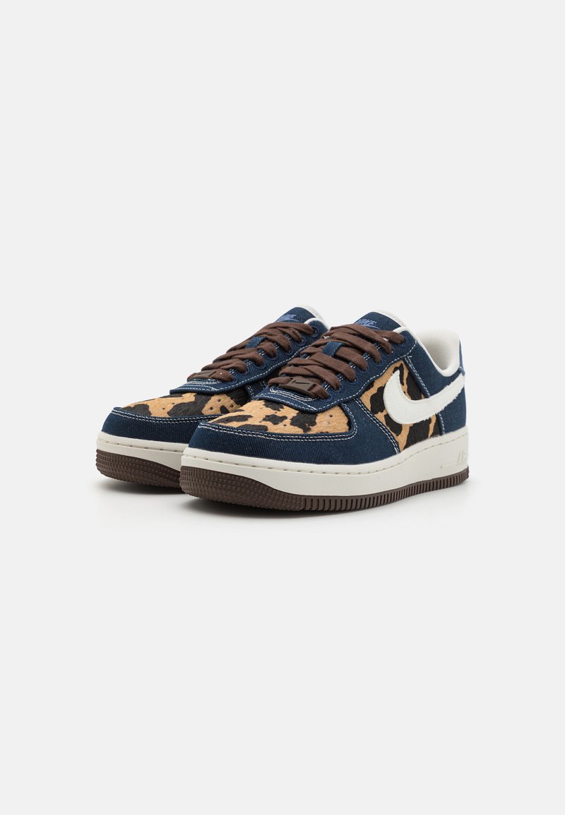 Blaue Sportschuhe mit einem braunen Schnürdesign, ausgestattet mit einem tanfarbenen gepunkteten Muster und dem weißen Nike-Swoosh, mit einer strukturierten Gummisohle.