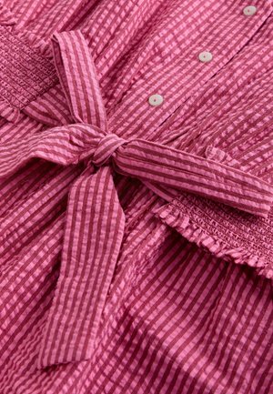 Pink striped fabric with a textured finish. Features a tie belt and buttons, adorned with ruffled accents at the top.