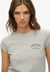 T-shirt gris à manches courtes en mélange de coton, avec un logo imprimé bleu sur le devant indiquant "SUPERDAY N.Y.C. Essentials Athlétiques".