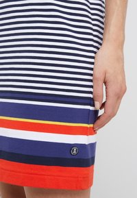 Gestreiftes Jersey-Kleid mit abwechselndem Marineblau und Weiß, mit einem bunten Saum in Rot, Gelb und Orange. Zeigt ein Markenlogo am Saum.