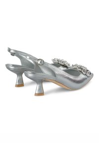 Dei tacchi slingback argento con una finitura metallica lucida, decorazioni decorative sulla parte anteriore e un design a tacco basso e svasato.