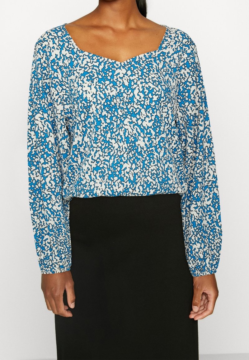 Blusa a maniche lunghe blu e bianca con un motivo e scollatura a V. Tessuto di cotone con una vestibilità ampia, che termina poco sopra la vita.