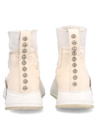 Vita ankelkängor i texturerad läder, med vadderat innertyg och en bakknapp med sex silverfärgade nitar. Gummisulor för bättre grepp.