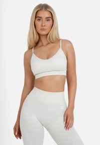 Hellbeige Sport-BH mit dünnen Trägern und einem verkürzten Design, kombiniert mit hoch taillierten Leggings mit strukturierten Akzenten und einem dezenten Logo.