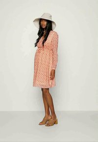 Vestido floral rosa com mangas longas, cintura franzida e caimento solto, combinado com um chapéu branco de aba larga e sapatos de salto aberto em tom bege.