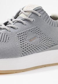 Baskets en maille gris clair avec une tige texturée et respirante, dotées d'une semelle intermédiaire blanche et d'une semelle extérieure en caoutchouc beige. Détail logo argenté inclus.