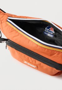 Πορτοκαλί τσαντάκι μέσης K-Way με μαύρη τσέπη με φερμουάρ και ανοιχτό κύριο διαμέρισμα που δείχνει το μαύρο εσωτερικό και την ετικέτα της μάρκας στο εσωτερικό.