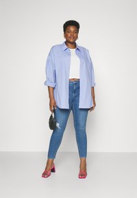 Lyseblå oversized skjorte med rullede ermer, hvit crop top, slitte blå jeans og rosa høye hæler. Svart veske som accent.