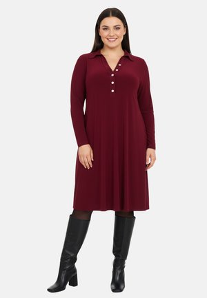 Burgunderfarvet langærmet kjole med krave og knaplukning, lavet af blødt stof, parret med sort knælang boots.