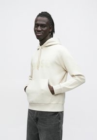 Κρεμ χρωματιστό φούτερ με απαλό ύφασμα, που διαθέτει μεγάλη μπροστινή τσέπη, κουκούλα με κορδόνι και διακριτικό ανάγλυφο λογότυπο "BOSS" στο στήθος.