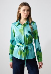 Cămașă cu mânecă lungă în turcoaz cu un model floral în acuarelă verde, cu închidere cu nasturi în față, guler ascuțit și o curea din același material la talie.