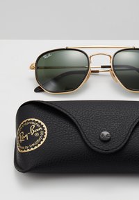 Ray-Ban sunglasses with dark green lenses, gold metal frame, and black textured case featuring a gold logo and button closure.
