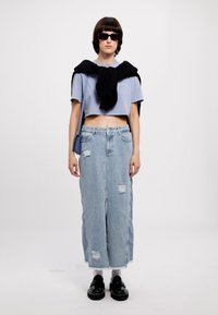 Light blue cropped t-shirt, black sweater tied around neck, light wash ripped denim skirt, black platform shoes, dark sunglasses.