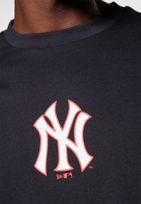 Marinblå t-shirt med kort ärm som har en vit och röd New York Yankees-logga. Slät, stretchig tyg med en klassisk rund halsringning.