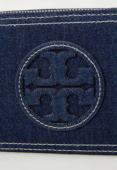 Carteira em denim com uma superfície texturizada azul-escuro, costuras brancas em contraste e um design de logotipo circular em relevo.