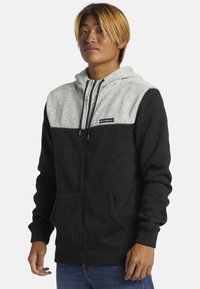 Hoodie zippé en gris et noir. Présente un haut texturé avec une moitié inférieure unie, des poches avant et une capuche avec cordon de serrage.